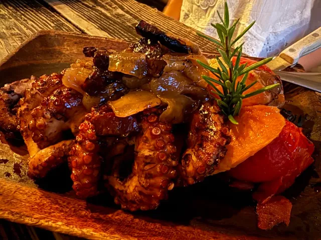 Grilled octopus arms with onion and red pepper on a wooden board, and a rosemary sprig