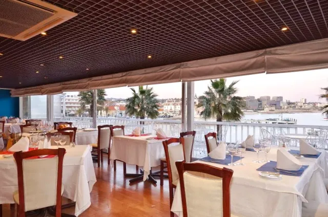 A room with white clothed tables and wide windows onto palm trees and a bay