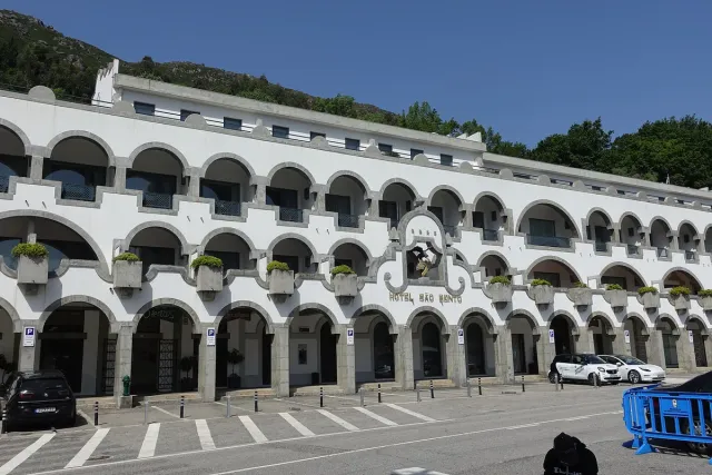 A white pilgrimage building with two tiers of arches facing a wooded slope