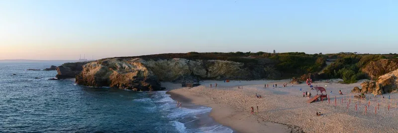A sandy cove ringed by low cliffs with white surf in soft late light