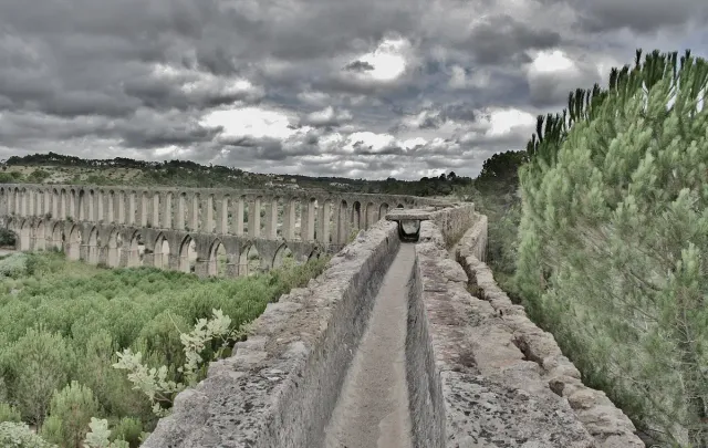 A stone water channel running along a long arcade of arches between shrubs