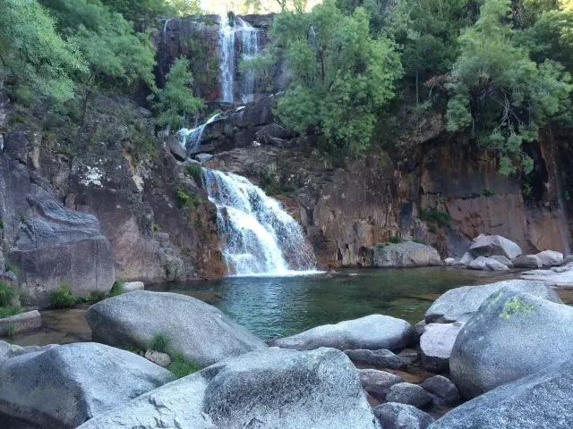 A tiered waterfall dropping between boulders into a clear natural pool