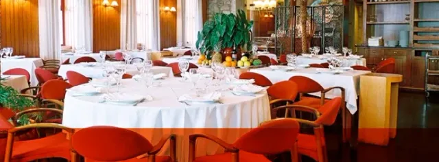 Round tables in white cloths with red chairs and greenery in the background