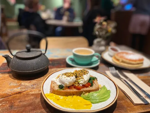Toast with poached eggs and avocado beside an iron teapot and a coffee cup
