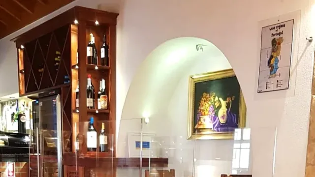 A wooden cabinet with wine bottles and a framed still life picture in a white alcove