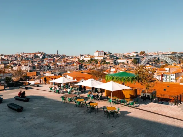 A raised plaza with parasols and green tables facing the city and the iron bridge
