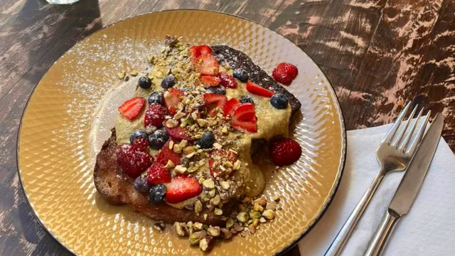 French toast on a golden plate with strawberries, blueberries and chopped pistachios