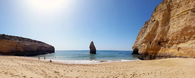 A sandy cove with a cliff and a lone rock in shallow water