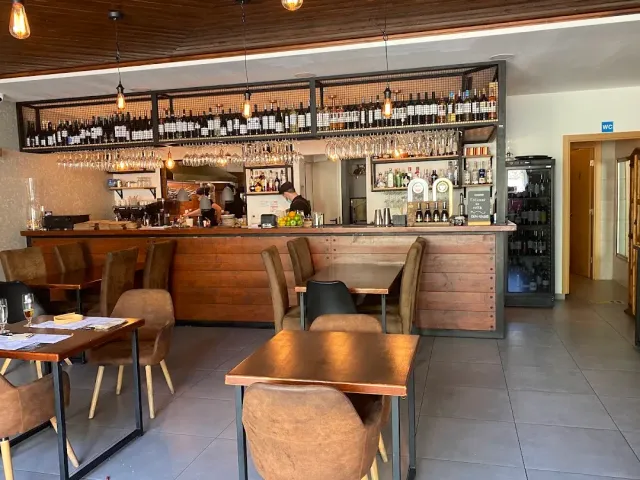 A wooden counter with a hanging wine bottle rack and upturned glasses above it