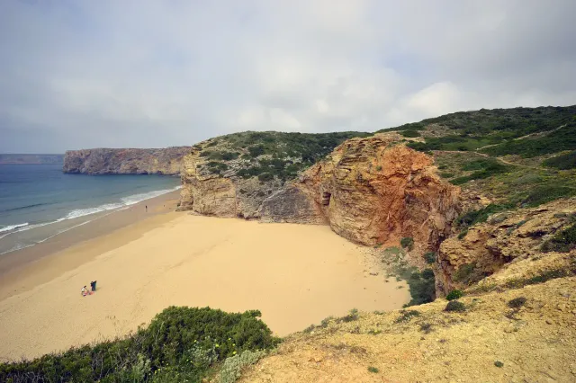 A sandy bay between tall reddish cliffs and blue sea
