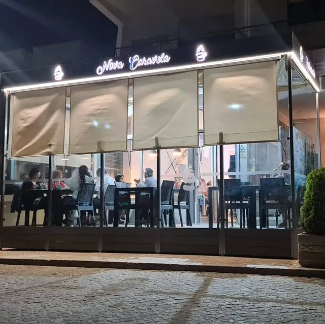 A facade lit at night with a glass wall, diners inside and an illuminated lettering sign