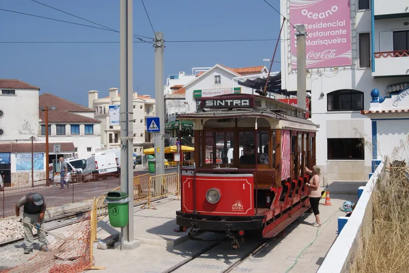 Old red and timber tram standing on street rails between white buildings