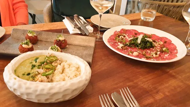 A bowl of green curry with rice, fried balls and carpaccio on a wooden table