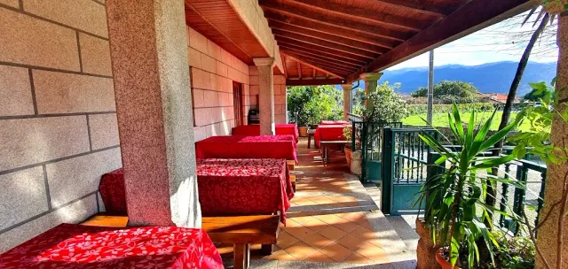 A covered terrace with red tablecloths, stone pillars and a view of fields and mountains