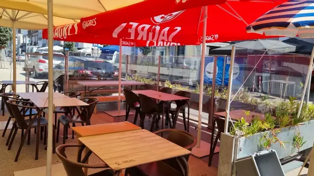 Outdoor tables under red parasols facing a road and a glass partition