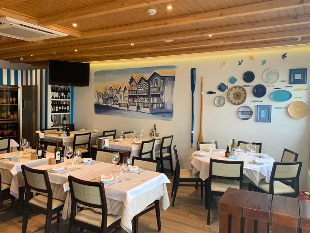 A room with a painting of striped houses on the wall, decorative plates and set tables