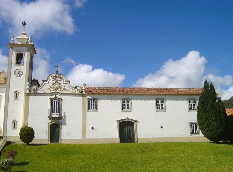 The chapel wing of the Doroteia sisters' convent, its bell tower carrying a clock and a weathervane cockerel above a baroque gable with a stone cross, a cypress and lawn beside it