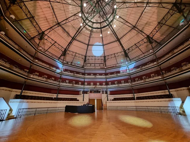 A round hall with a wooden floor, three tiers of balconies and an iron and glass dome