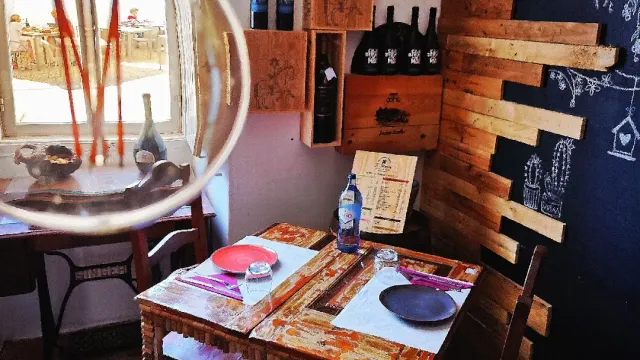 A painted wooden table corner with wine crates on the wall, a round mirror and a chalkboard