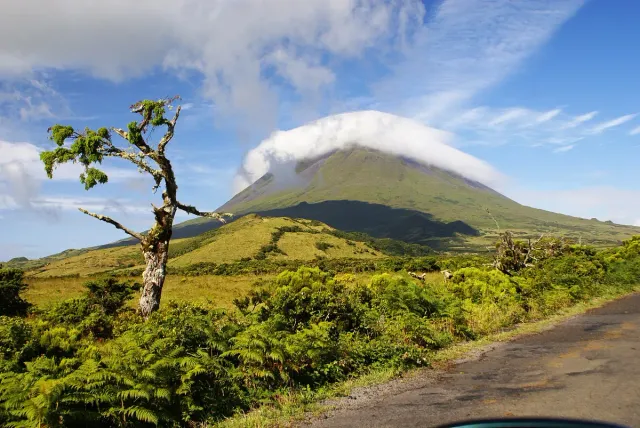 A cloud capped volcanic cone above green slopes