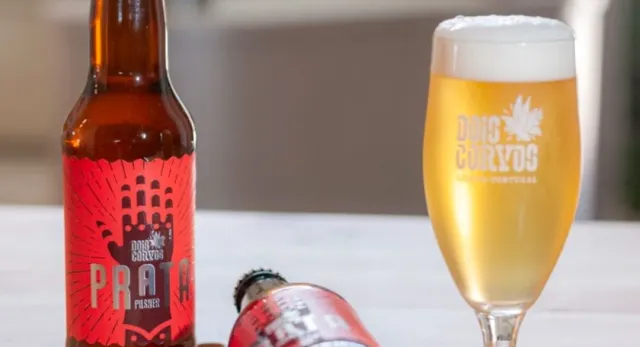A beer bottle with a red label beside a full goblet with white foam