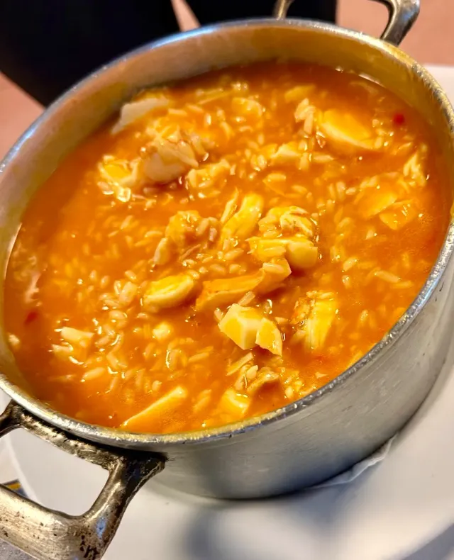 A metal pot full of rice in orange broth with white pieces of fish