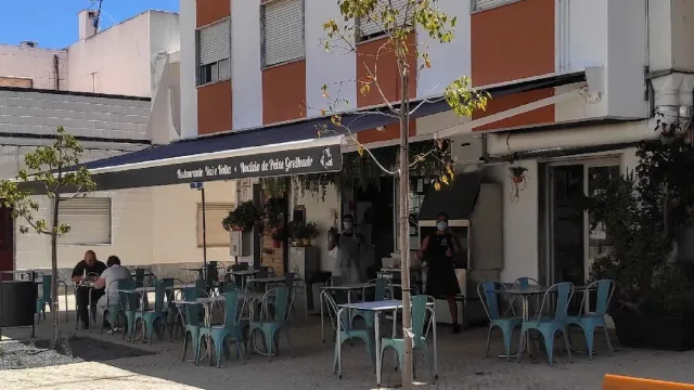 Turquoise metal chairs around tables on a street pavement, under a blue awning