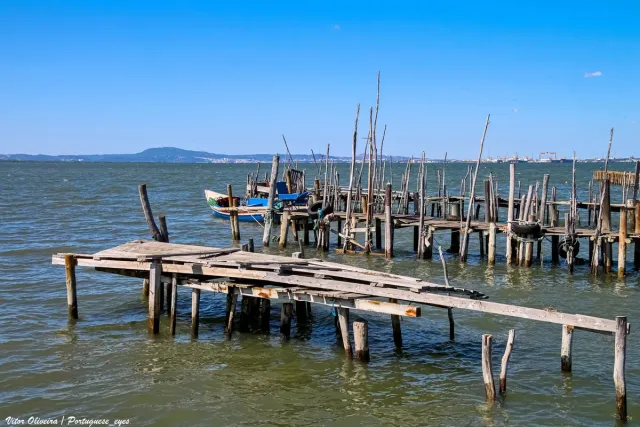 A rickety wooden pier on stilts over a shallow estuary with fishing boats