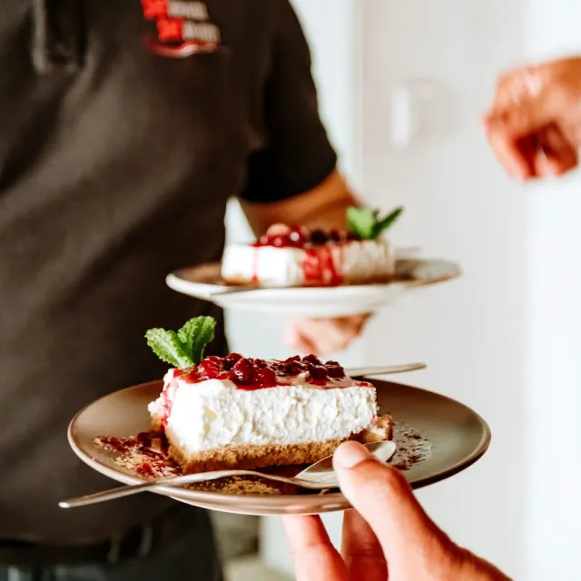 A waiter holding two plates of cheesecake with berry jam and a mint leaf