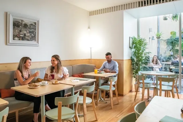 A bright space with an upholstered bench, mint-coloured chairs, and a leafy courtyard beyond the window