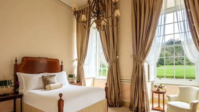 A classic bedroom with a chandelier, golden curtains and tall windows onto a lawn