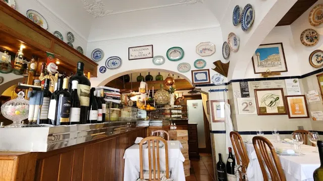 A small room with ceramic plates on the walls, wine bottles on the counter and framed certificates