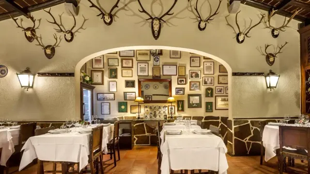 A room with antlers on the walls, a wall of framed pictures and white tables
