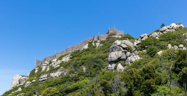 Crenellated fortress walls along a ridge above granite boulders and forest