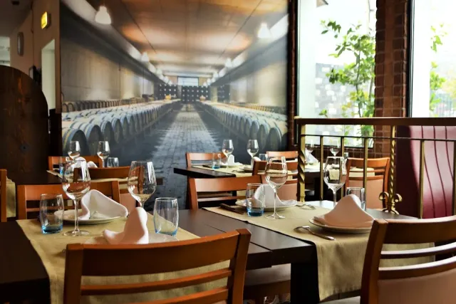 A dining room with set tables and wine glasses facing a wall photograph of a barrel cellar