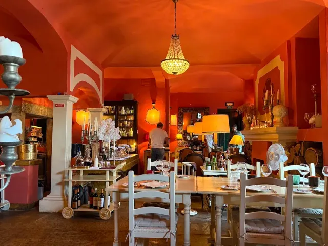 An orange toned room with a vaulted ceiling, a chandelier and white wooden tables and chairs