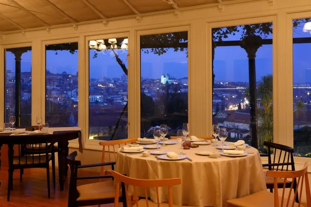 A set round table facing large windows with a lit city view in the evening