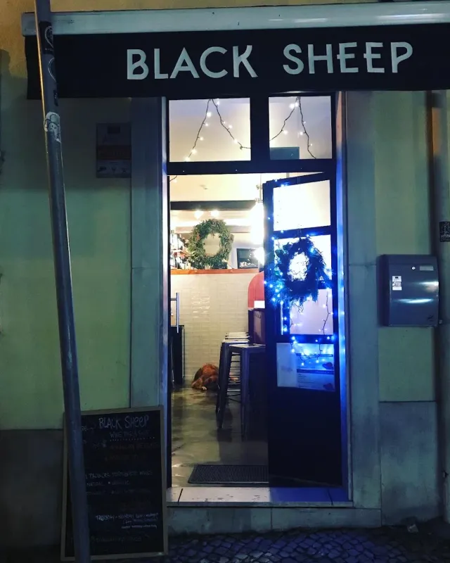 A small storefront at night with an open door, green wreaths and string lights