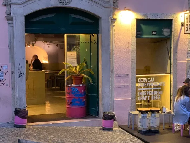 A pink facade with an open green gate, a flower barrel and evening lights