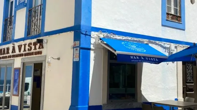 A white and blue facade with a blue awning and lettering set on the wall