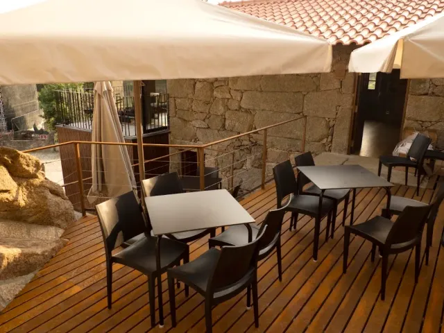 A wooden deck with pale parasols and dark chairs, beside a stone wall and a tiled roof