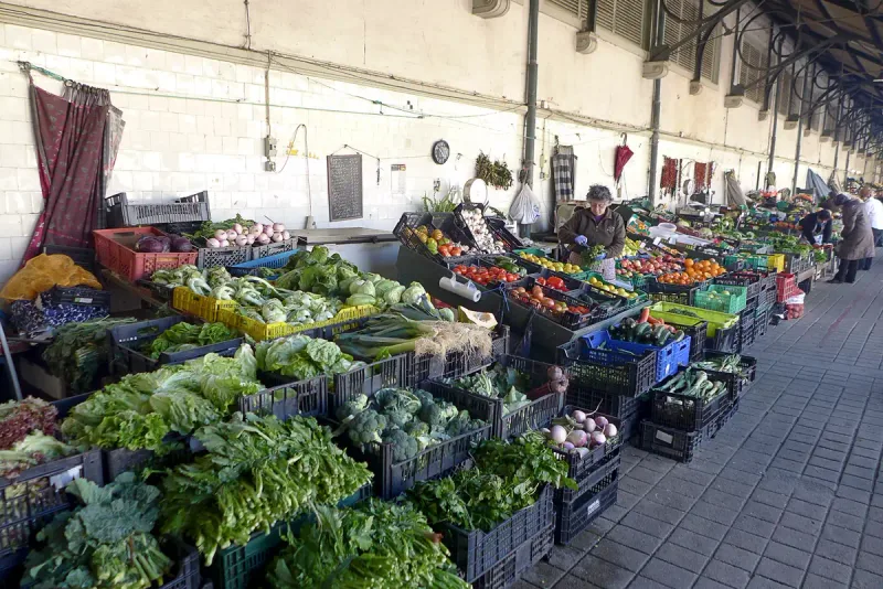 Vegetable stalls piled with fresh greens under the roof of a market hall