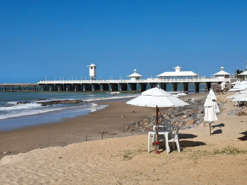 Sand and white parasols in front of a long wooden pier with white roofed pavilions