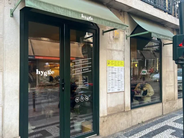 A cafe front with green frames, awnings and menu boards on the wall