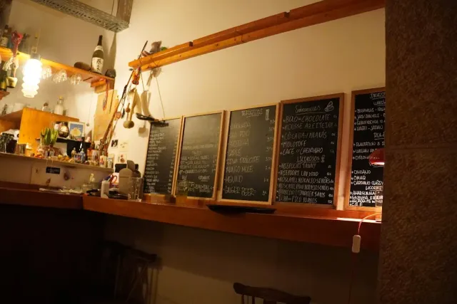 A wooden shelf with four written chalkboards, bottles and hanging objects