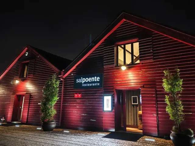 A wooden building lit in red at night with a lit entrance and shrubs in pots