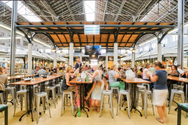A covered market hall with iron beams, communal tables and diners