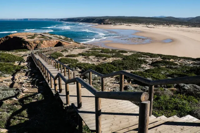A boardwalk descending to a vast dune beach with white surf