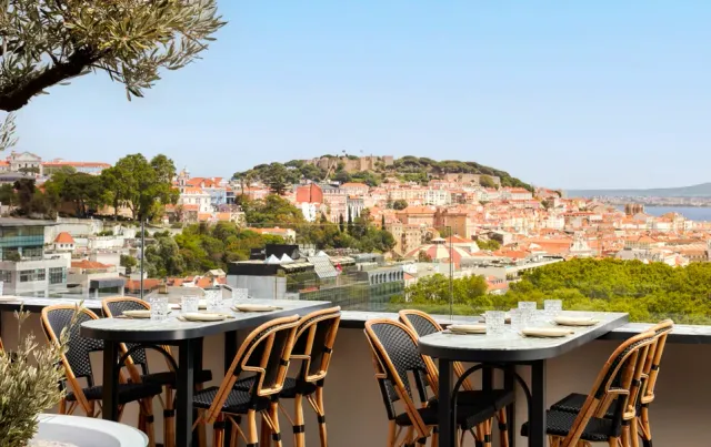 High tables and rattan chairs on a rooftop facing a hill with a castle