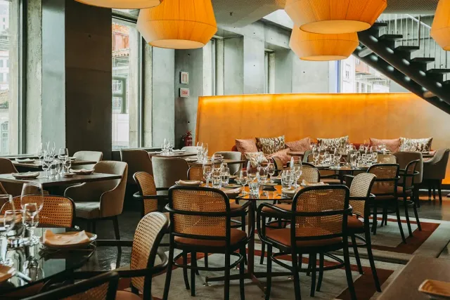 A dining room with large orange lampshades, cane chairs and a cushioned banquette